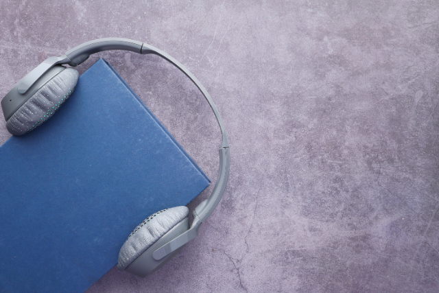 Un livre bleu repose sur une surface grise avec des écouteurs gris dessus.
