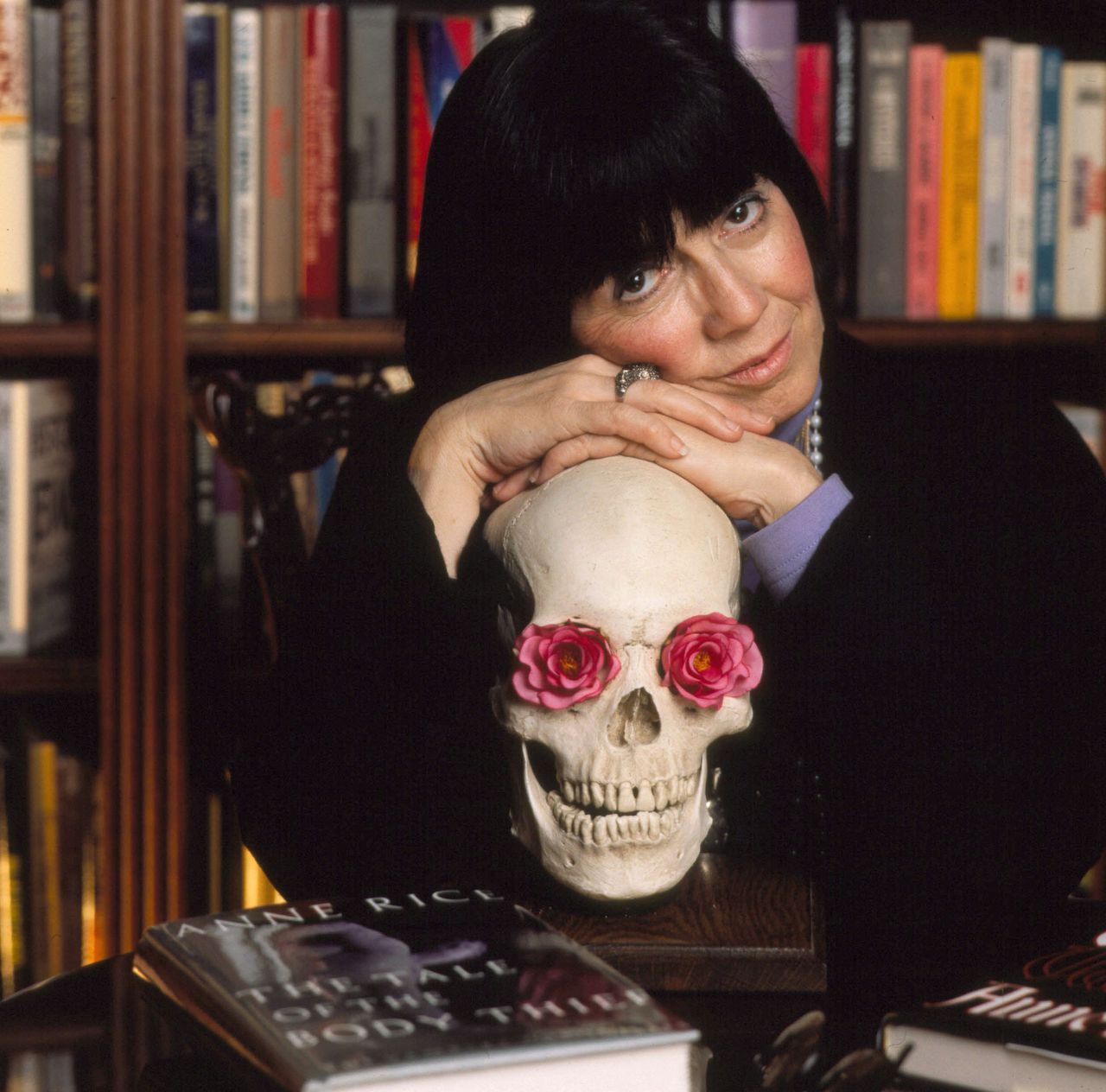 Anne Rice with her arms crossed over a skull with roses in the eyes