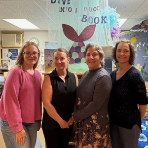 Quatre femmes se tiennent devant les étagères de la bibliothèque et sourient à la caméra