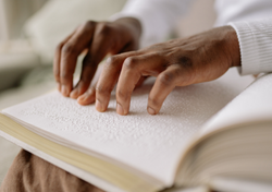 Two hands with dark skin touch a page of braille in a book.