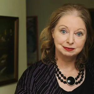 Portrait of Hilary Mantel. She is wearing a black top with white stripes and a necklace with black beads.