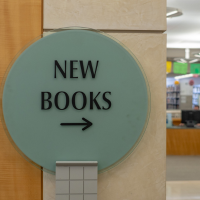 A round sign has the text New Books and an arrow pointing to library shelves in the background.