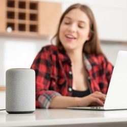 Une femme tape sur un ordinateur portable et écoute un haut-parleur intelligent.