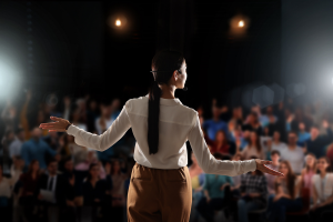 A woman stands on a stage in front of an audience.