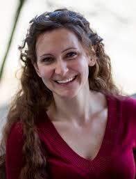 Image of author Amanda Leduc. She is smiling, and has long curly hair and a wine coloured top, 