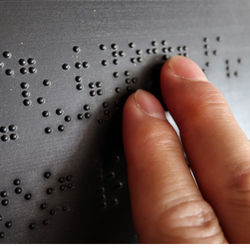 close up photograph of two fingers reading braille on a grey sign