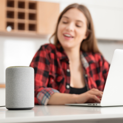Une femme tape sur un ordinateur portable et écoute un haut-parleur intelligent.