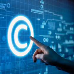the copyright symbol of the letter C surrounded by a circle is projected on a screen and a person's hand points towards the image. 