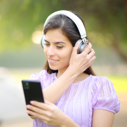 A woman is wearing headphones and holding her phone. 
