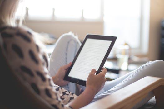 A woman in a spotted sweater reading a book on a tablet