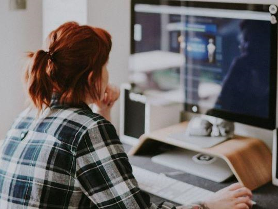 Red-haired woman in a plaid shirt seated at computer