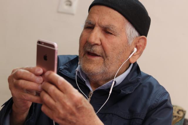 an elderly man in a knit cap listening to a book on an iphone