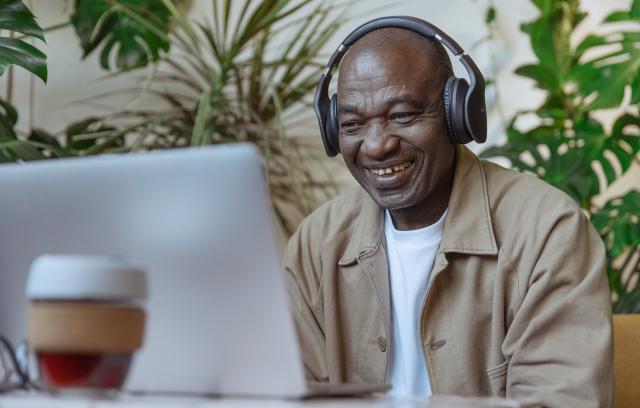 Black man with headphones watching video on laptop and smiling